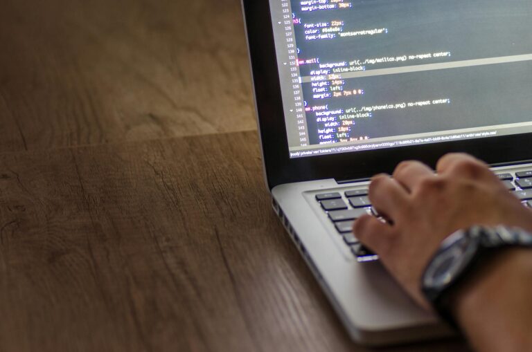 A person is typing code on a laptop, focusing on the screen with programming script.